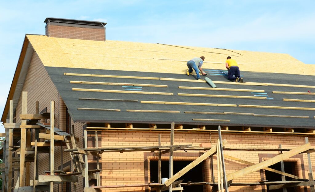 roof installation A close-up of a brick house under construction with the roofing contractors on unfinished rooftop installing roofing waterproofing rubberized asphalt underlayment before asphalt shingles installation.