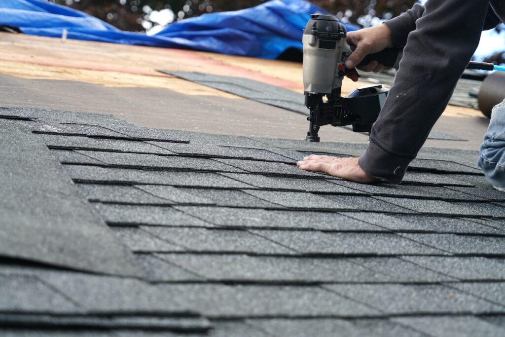 handyman using nail gun to install shingle to repair roof roof installation
