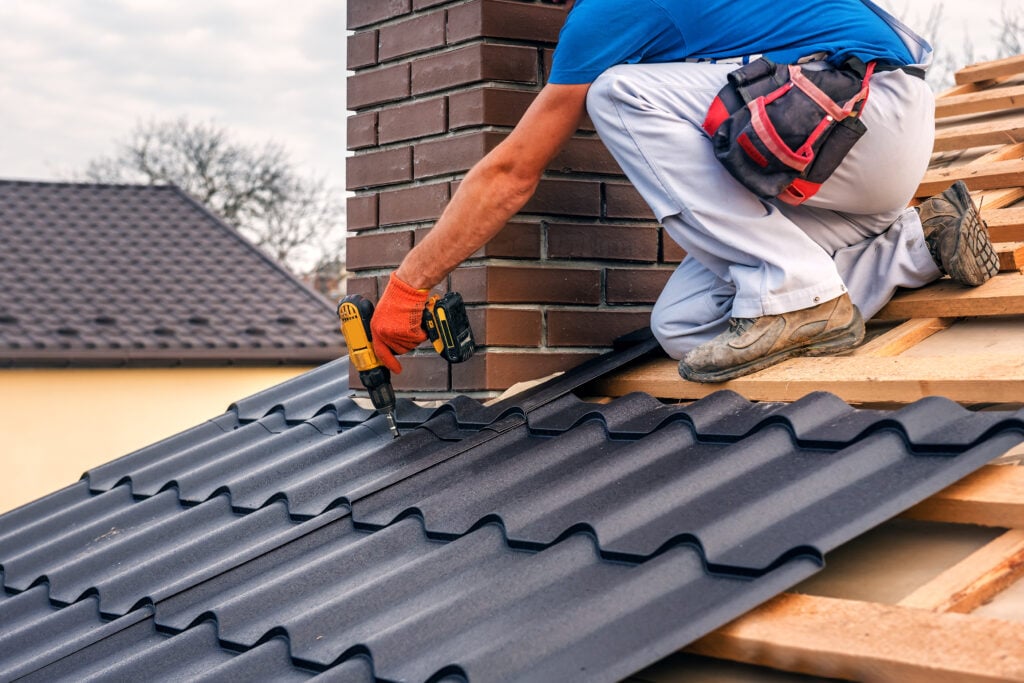 a professional master (roofer) with electric screwdriver covers repairs the roof near the chimney