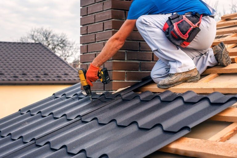 a professional master (roofer) with electric screwdriver covers repairs the roof near the chimney
