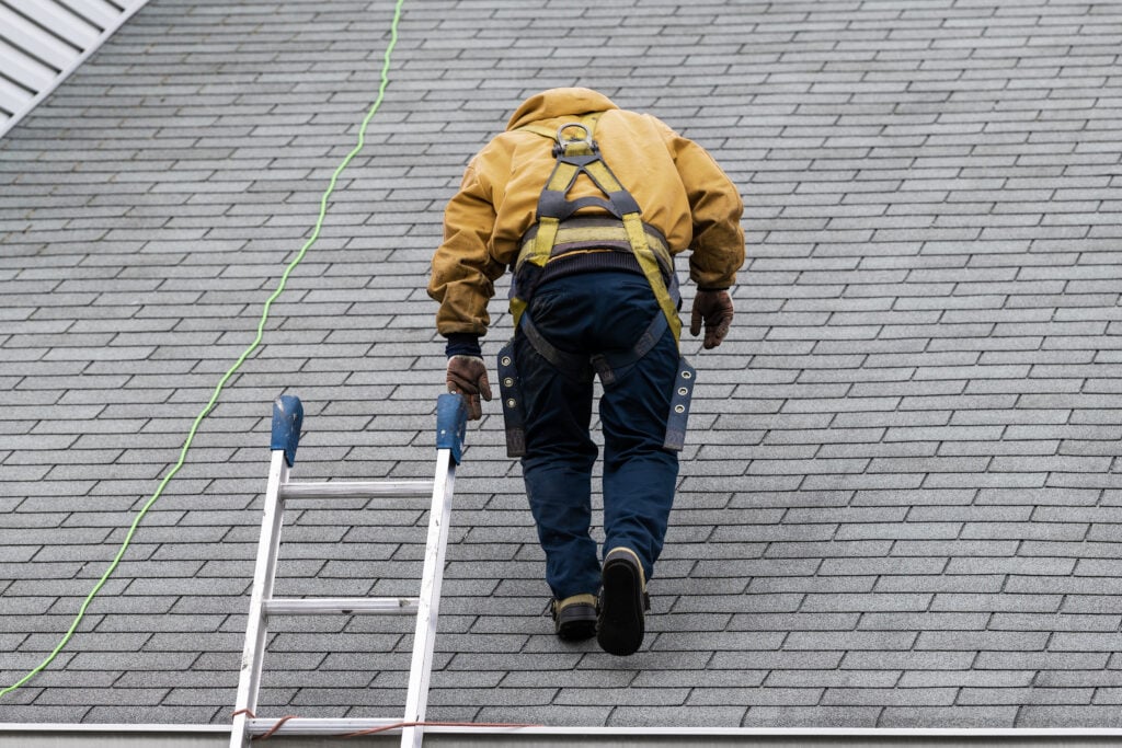 roof leak repair House during day with gray color Single Family Home and construction man in yellow uniform walking on roof shingles and ladder during repair