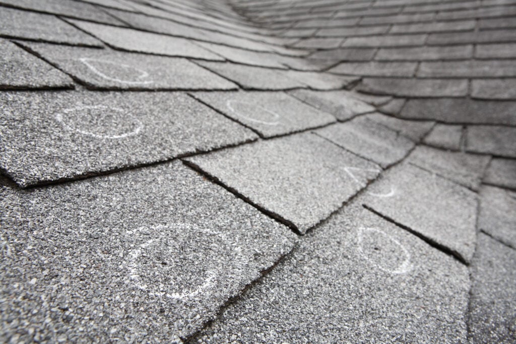 Old roof with hail damaged shingles, chalk circles mark the dama
